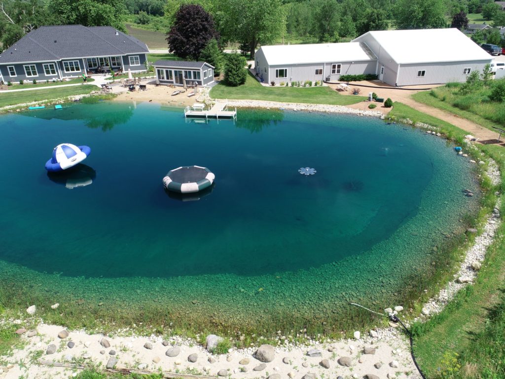 Aerial view of ultimate backyard transformation pond with fountain, pier/dock, and inflatables