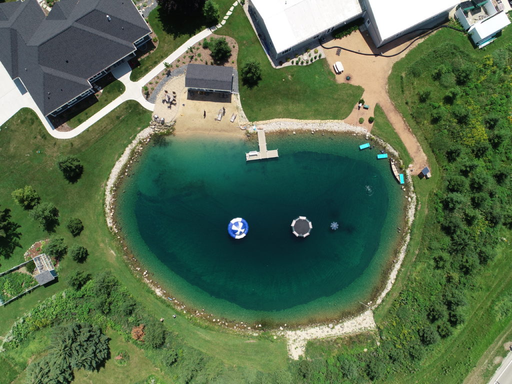 Backyard swim pond aerial view with fountain, pier/dock, beach, and inflatables